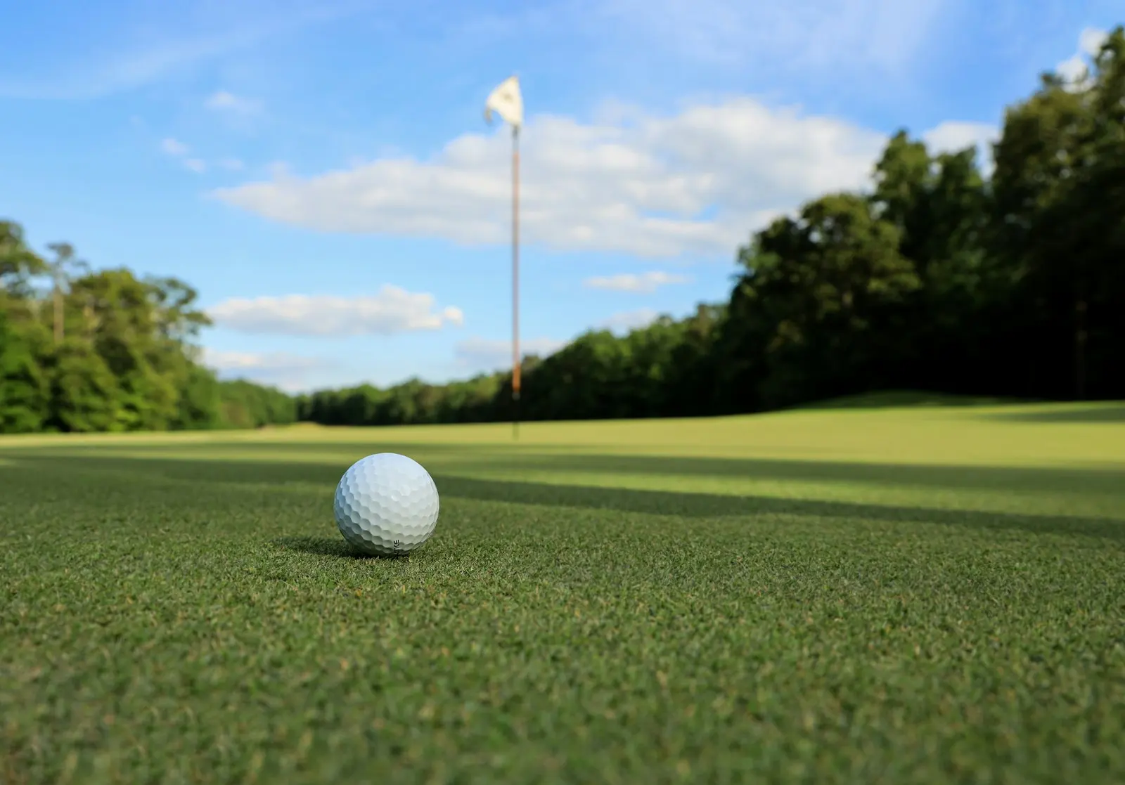 A golf ball resting on a putting green with the flag and a blue sky beyond