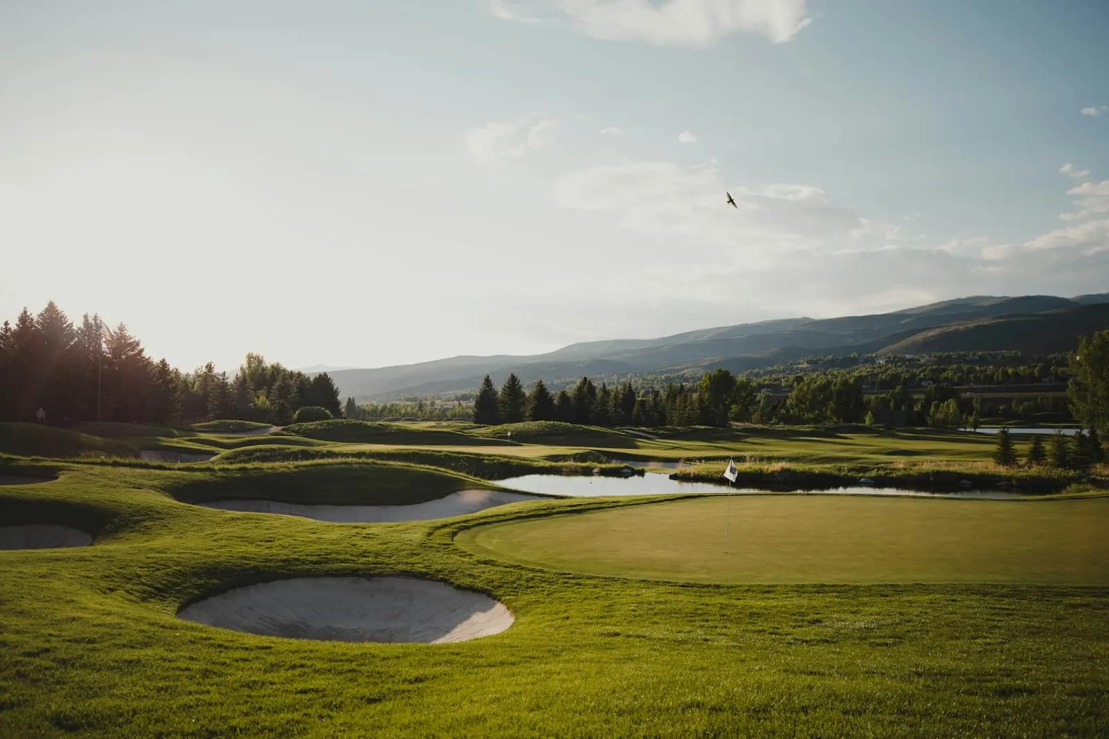 Golf course at dusk with bunkers, a green, and mountains beyond